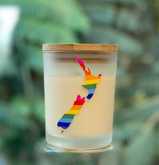 Frosted glass soy candle with a cork lid and rainbow New Zealand map design, photographed against a soft green background.