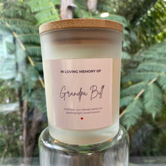 A memorial candle in a frosted glass jar with a bamboo lid, The candle features a light pink label that reads 'IN LOVING MEMORY OF Grandpa Bull'.