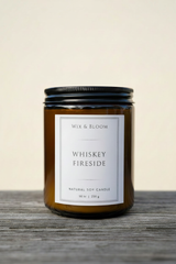 Whiskey Fireside Natural Soy Candle in amber jar on rustic wood with cream background