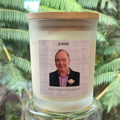 A personalized memorial candle in a frosted glass jar with a bamboo lid, featuring a custom photo label that reads 'In Loving Memory' 