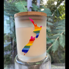 Frosted glass soy candle with a cork lid and rainbow New Zealand map design, photographed against a soft green background.